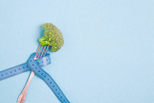one broccoli on a fork wrapped in blue measuring tape on a blue background place copy top view diet and weight loss concept - Фото, зображення
