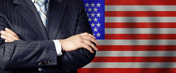 Επιχειρηματίας με κοστούμι με τα χέρια σταυρωμένα σε φόντο σημαίας - Φωτογραφία, εικόνα