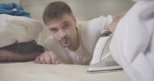 Close-up of blurred young man ironing laundry with iron. Focused on household utility. Handsome brunette Caucasian guy doing housework. Housekeeping, lifestyle, hygiene. Cinema 4k ProRes HQ. - Filmati, video