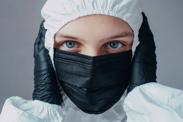 Virologist in a viral protective suit and medical mask holding his hands in black gloves and thinking about the consequences of the coronavirus epidemic. Doctor thinks how to stop virus. - Foto, Bild