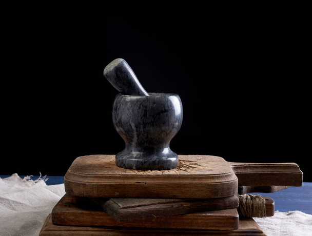 black stone mortar with pestle for grinding spices and herbs on a brown wooden board, black background - Фото, зображення