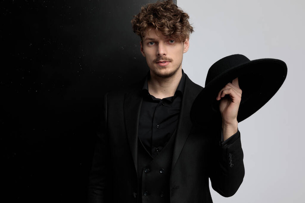 Bájos divat modell forog egy kalap az ujján, miközben öltönyt visel, és áll a fekete-fehér stúdió háttér - Fotó, kép