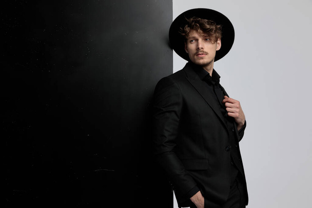 Umfangreiches Mode-Model schaut weg, während es Anzug und Hut trägt, steht auf schwarz-weißem Studiohintergrund - Foto, Bild