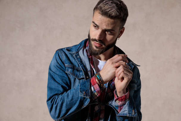 Afraid model looking away and holding hands together while wearing jeans jacket and standing on wallpaper studio background - Fotoğraf, Görsel