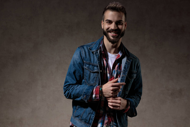 Cheerful model laughing while wearing jeans jacket and standing on wallpaper studio background - Фото, изображение