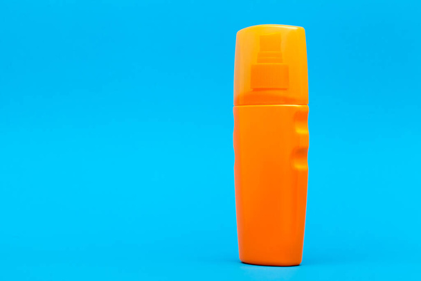 orange plastic bottle of suntan cream side view on a blue background with copy space. - Φωτογραφία, εικόνα