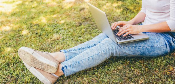 Freelance business concept. Woman legs on green grass lawn in city park, hands working on laptop pc computer. Lifestyle authentic candid student girl studying outdoors. Mobile Office - Φωτογραφία, εικόνα