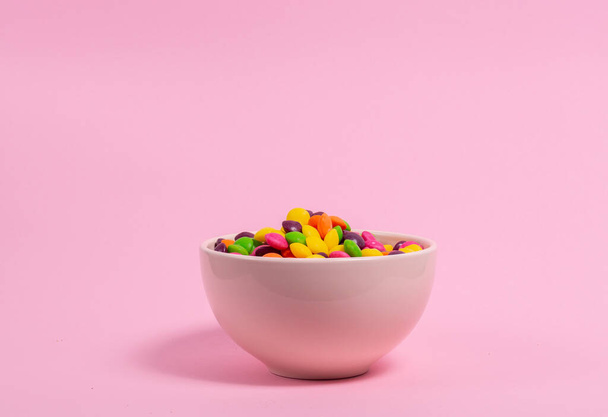 Schüssel voller farbiger Bonbons auf rosa Hintergrund - Foto, Bild
