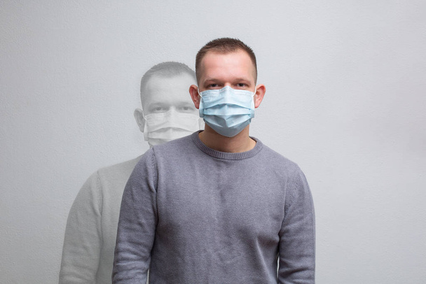 Ένας άντρας με ιατρική μάσκα κοιτάζει την κάμερα σε ουδέτερο φόντο. - Φωτογραφία, εικόνα