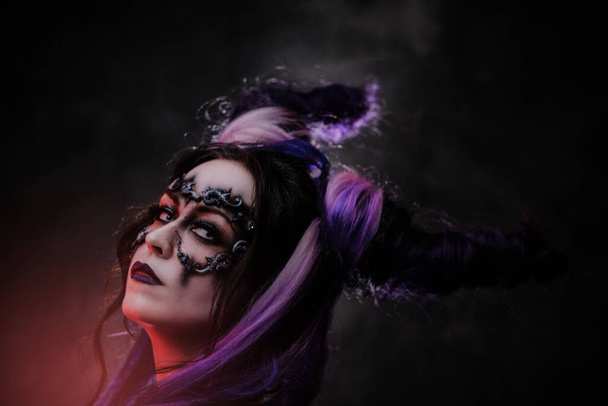 Cosplayer girl wearing dark mythical make up and horns posing in a studio on a dark background with red light - Fotoğraf, Görsel