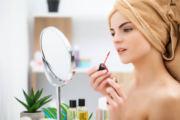 Jolie jeune femme met du maquillage sur le visage dans la salle de bain - Photo, image