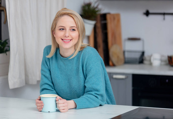 senhora loira com xícara de café na cozinha
  - Foto, Imagem