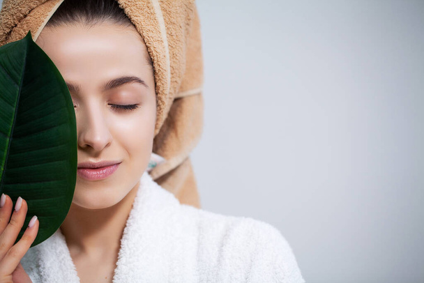 Chica bonita con una toalla en la cabeza y una hoja verde después de tomar una ducha
 - Foto, Imagen