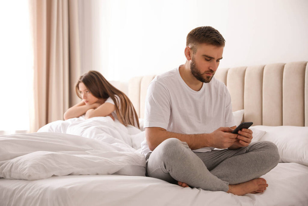 Young man preferring smartphone over his girlfriend on bed at home. Relationship problems - Fotoğraf, Görsel