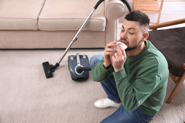 Man with vacuum cleaner suffering from dust allergy at home - Photo, Image