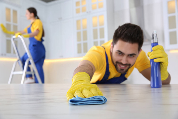 Professional young janitor cleaning table in kitchen - Foto, Bild