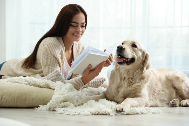 Young woman with book and her Golden Retriever at home. Adorable pet - Photo, image