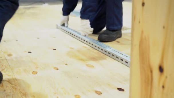 In einem großen Raum auf dem Holzboden tragen zwei Arbeiter Overalls, weiße Handschuhe ziehen gerade Linie und markieren mit glatten langen Metallteilen oder Rohlingen, während sie sie neu anordnen. Nahsicht in Innenräume. - Filmmaterial, Video