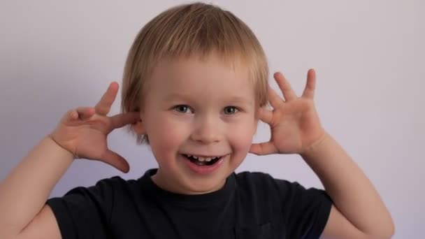 Portrait of happy cheerful little boy posing playing hands near ears laughing having fun - Felvétel, videó