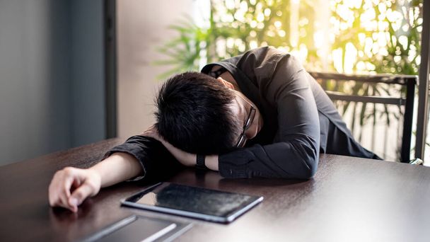Empresário asiático sobrecarregado dormindo na sala de reuniões do escritório com tablet digital na mesa de conferência. Exaustão e problemas de saúde decorrentes do conceito de sobrecarga de trabalho
 - Foto, Imagem