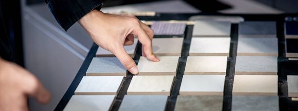 Male architect or interior designer hand choosing ceramic texture sample from swatch board in design studio. Floor and wall finishing material for architecture and construction industry. - Foto, Imagen