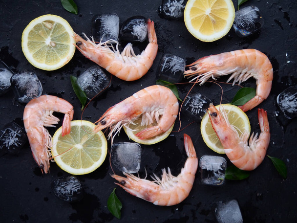 Fresh shrimps with rosemary or basil spices, lemon and ice on a black stone board plate. Top view of seafood ingredients. - Fotoğraf, Görsel