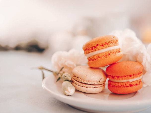 French macaroon cakes. Macaroons on a white plate with flowers on gray table background. Selective focus - Zdjęcie, obraz
