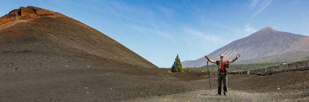 Viajante com bengala e câmera fotográfica perto do Vulcão Arenas Negras e campos de lava ao redor. Céu azul brilhante e nuvens brancas. Parque Nacional Teide com vulcão Teide ao fundo. Tenerife
. - Foto, Imagem