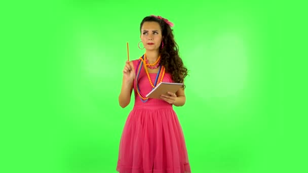 Girl stands and thinks, then writes with pencil in notebook and gets angry. Green screen - Video