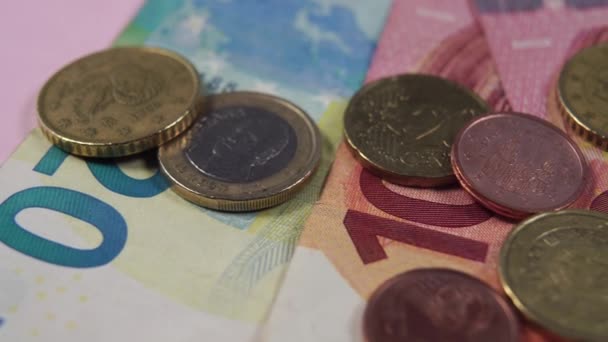 Billetes y monedas en euros en primer plano sobre un fondo rosa. Dolly macro disparo
. - Imágenes, Vídeo