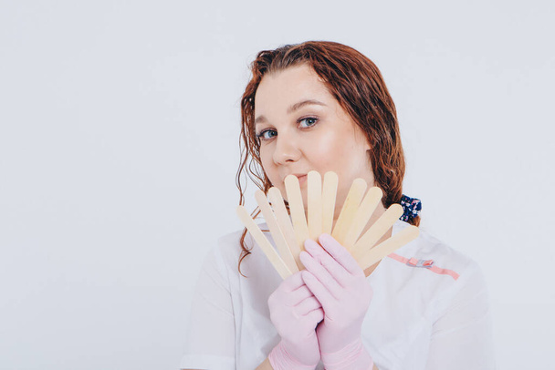 a girl in a white coat with wooden sticks in her hands. the doctor is preparing for waxing. Medicine concept, medical instruments, health care , beauty industry, hair removal, natural material - Photo, image