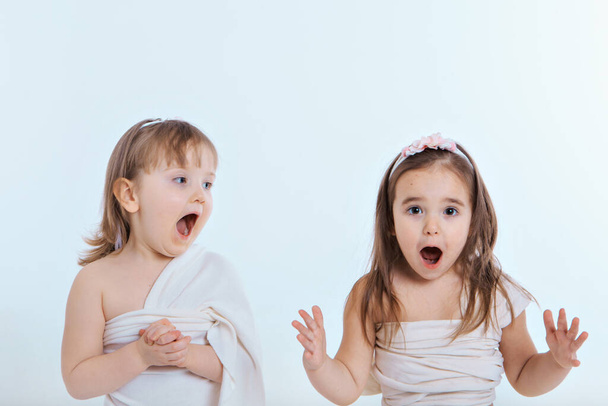 two little girls with their mouths wide open on a white background. The children are playing. the concept of education , childhood, emotions, dentistry, surprise, friendship. Copy space - Fotografie, Obrázek
