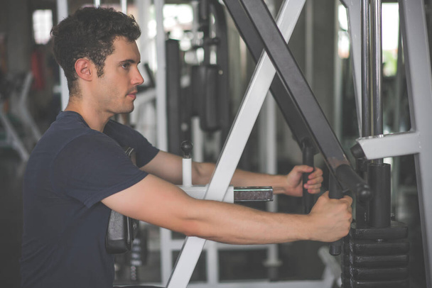 Beau homme abaissant le poids de la machine de remise en forme et de l'exercice dans la salle de fitness. - Photo, image