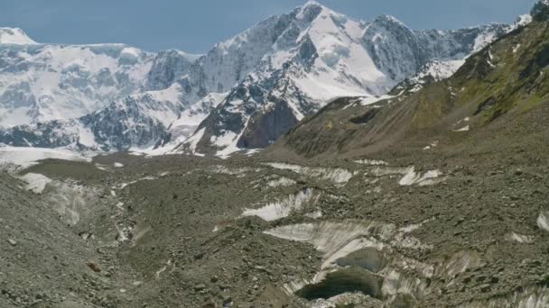 Snowy mountain towers above glacier tongue, melt water flows over rocky riverbed - Footage, Video
