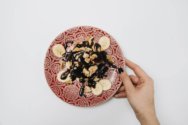 Stapel heerlijke zelfgemaakte pannenkoeken met chocolade topping, walnoten en gesneden bananen - Foto, afbeelding