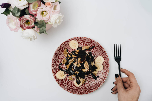 Стопка вкусных домашних блинчиков с шоколадной начинкой, грецкими орехами и нарезанными бананами
 - Фото, изображение