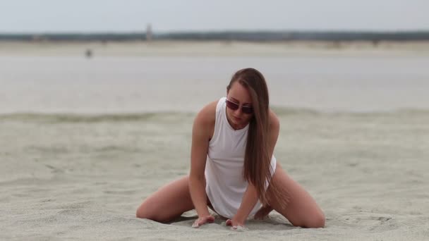 Languid kobieta siedzi Cross-legged na piasku dotykając skóry - Materiał filmowy, wideo