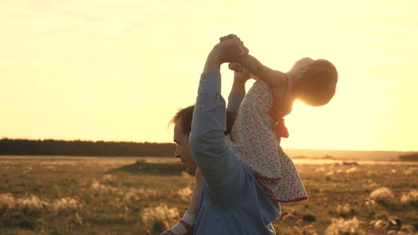 Tata z ukochaną córką na ramionach tańczy w locie i śmieje się. Szczęśliwe dziecko bawi się z ojcem na polu zachodzącego słońca. Sylwetka mężczyzny i dziecka. Pojęcie rodziny i dzieciństwa - Zdjęcie, obraz