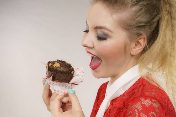 Sweet food sugar make us happy. Attractive blonde woman holds yummy chocolate cupcake in hand, open mouth, craving for cake. - Photo, image