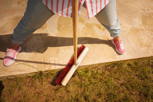 Person using big broom to clean up backyard patio. Housecare duties concept. - Фото, изображение