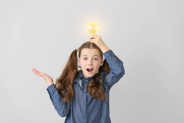 Cute little schoolgirl with glowing light bulb on grey background - Photo, Image