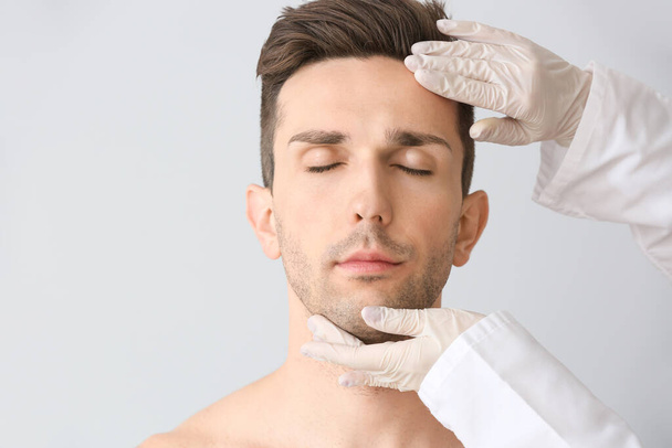 Cirujano plástico tocando la cara del joven sobre fondo claro
 - Foto, imagen