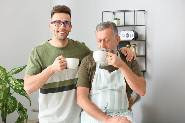 Portrait de l'homme âgé et son fils adulte buvant du thé dans la cuisine
 - Photo, image