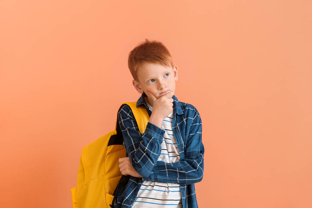 Nachdenklicher kleiner Junge mit Rucksack auf farbigem Hintergrund - Foto, Bild