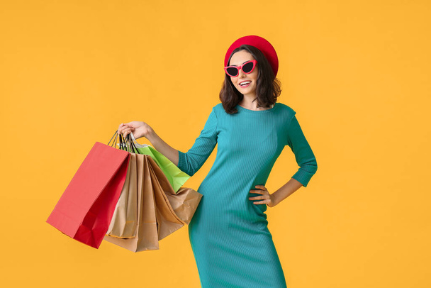 Όμορφη νεαρή γυναίκα με τσάντες ψώνια στο φόντο χρώμα - Φωτογραφία, εικόνα