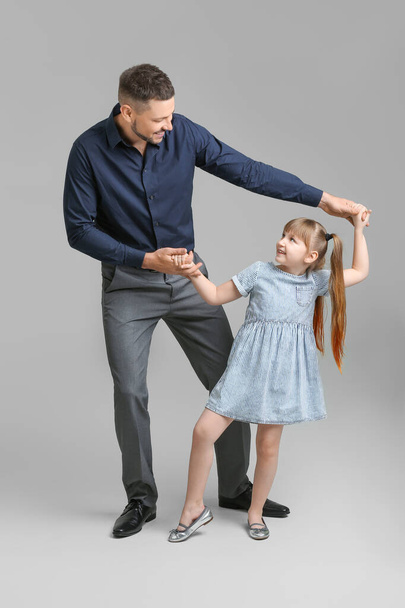 Father and his little daughter dancing against grey background - Zdjęcie, obraz