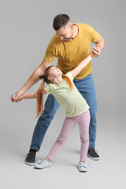 Father and his little daughter dancing against grey background - Photo, Image