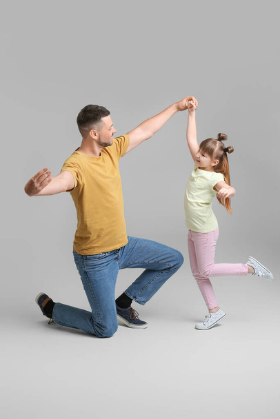 Father and his little daughter dancing against grey background - Fotoğraf, Görsel