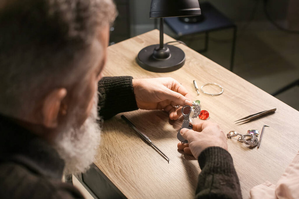 Jeweller examining adornment in workshop - Φωτογραφία, εικόνα
