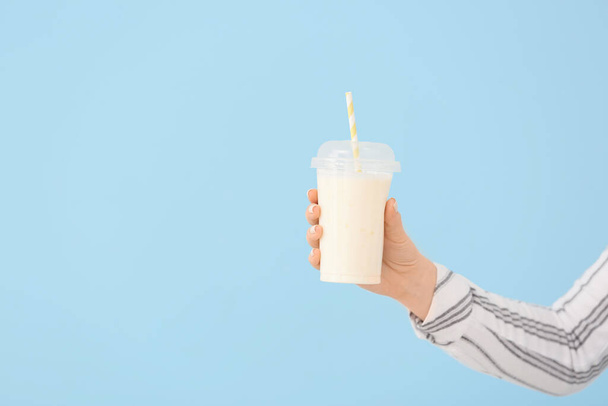 Mão feminina com xícara de saboroso milkshake no fundo de cor
 - Foto, Imagem